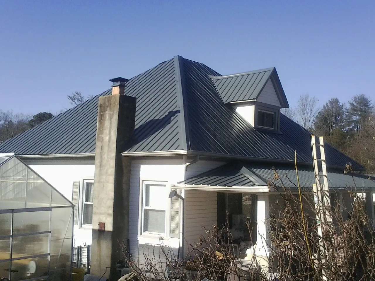 Dark blue standing seam metal roof on a white farmhouse with dormer — Slate & Tile Roof Repair by Roofing Brothers in Hector