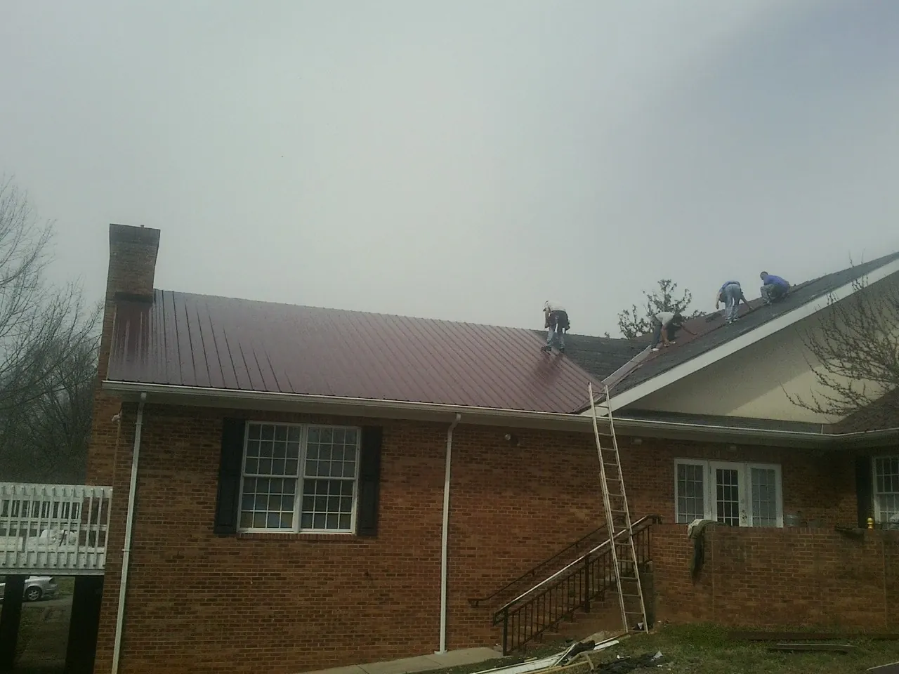 Crew setting red metal roofing panels on a brick home in Hector