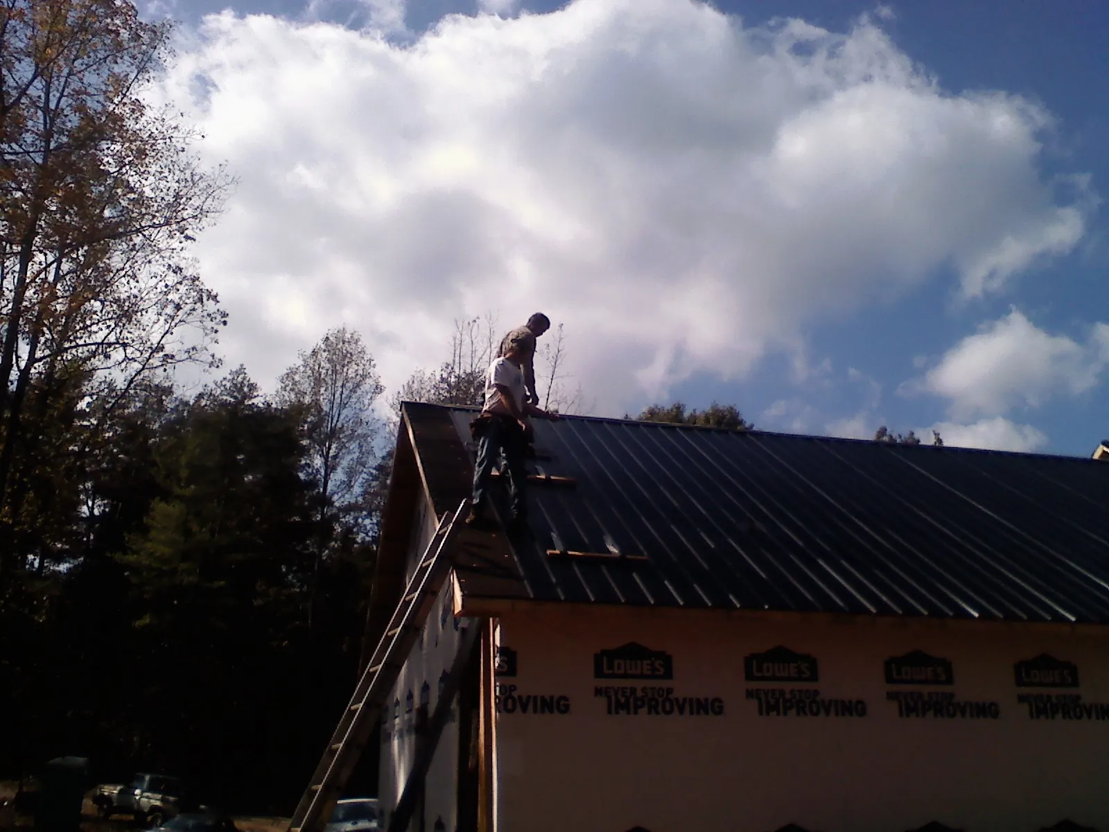 Roofer fastening dark metal panels high against a cloudy sky, from a Roof Inspection job in Hector