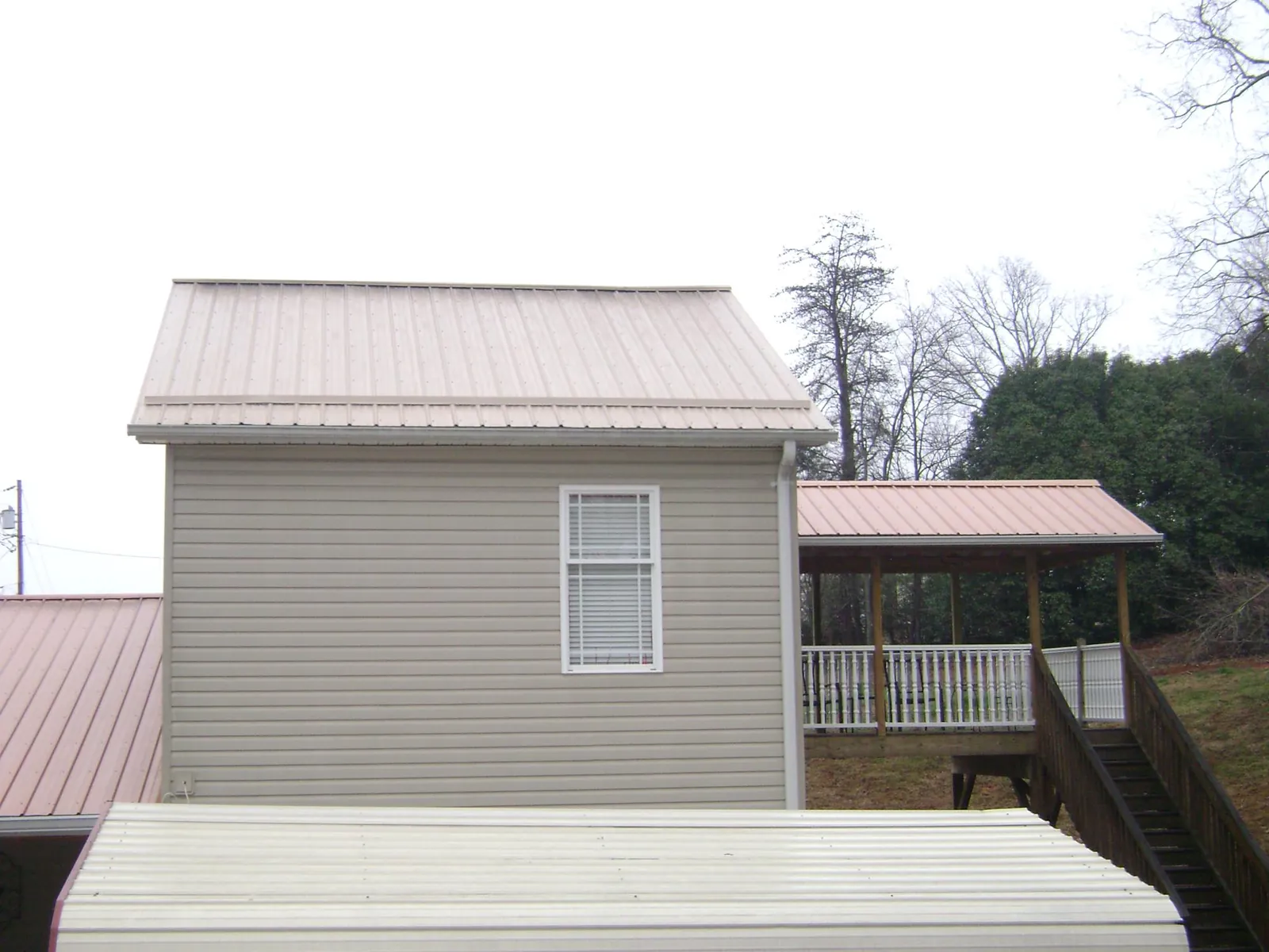 Tan metal roofs on a two story addition and attached porch, from a Roof Replacement job in Hector